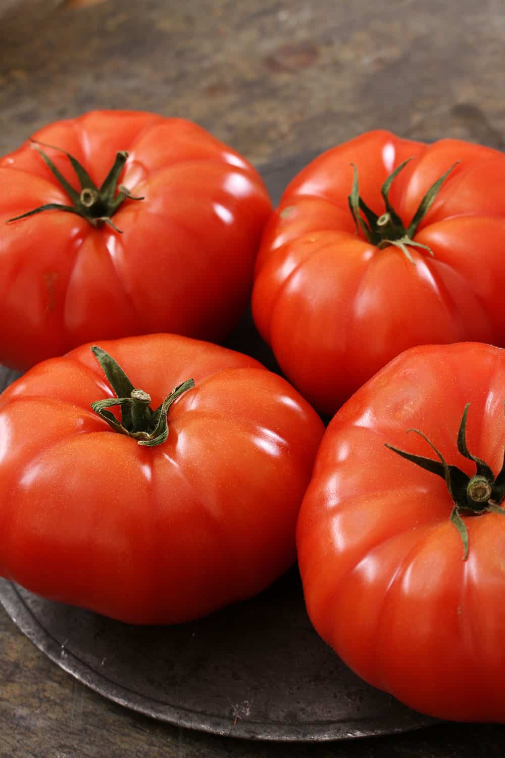 Four ripe beefsteak tomatoes sitting next to each other on a brown plate. 