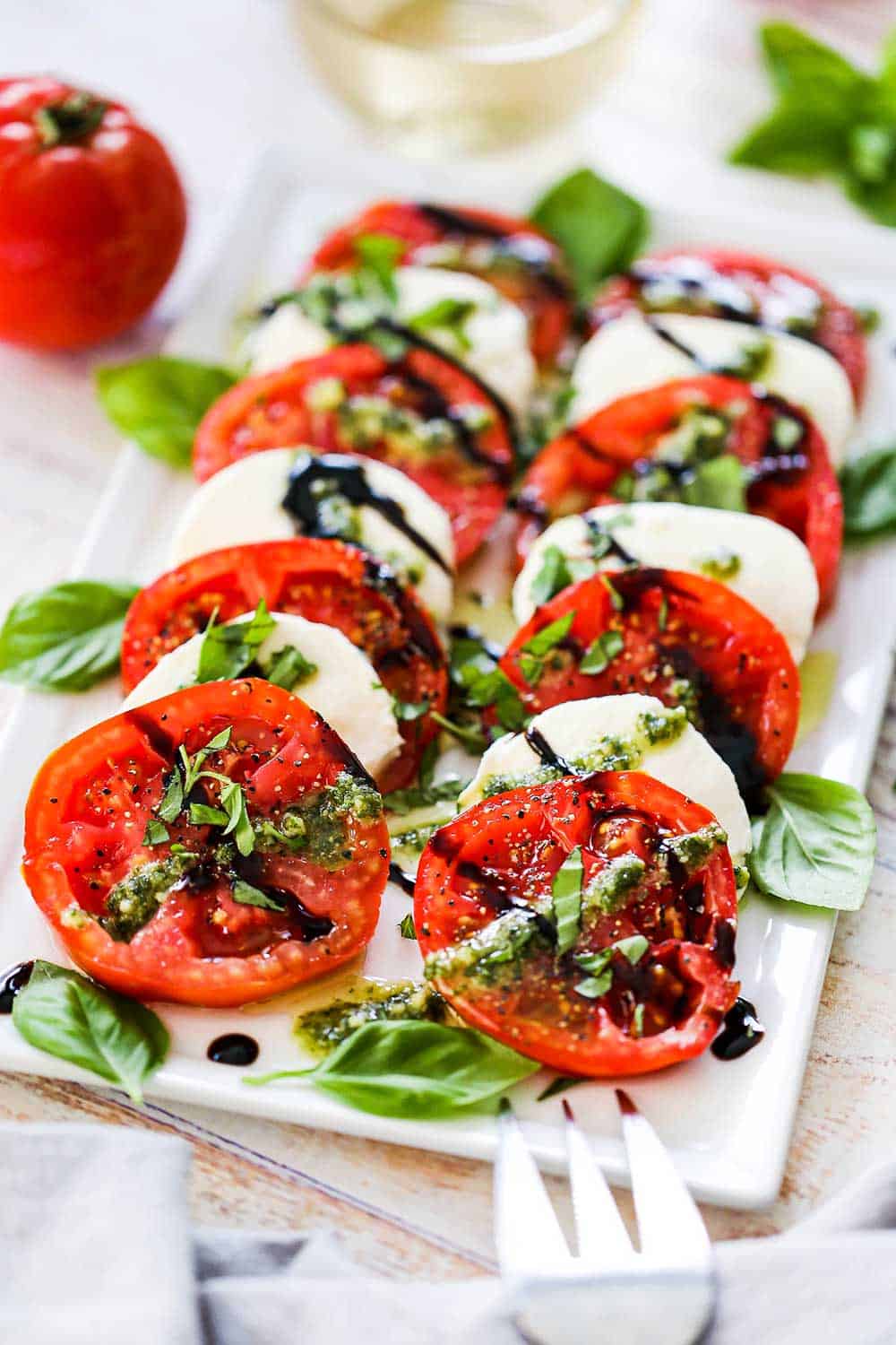 A platter of caprese salad that has been drizzled with pesto sauce and a balsamic glaze and topped with freshly chopped basil.