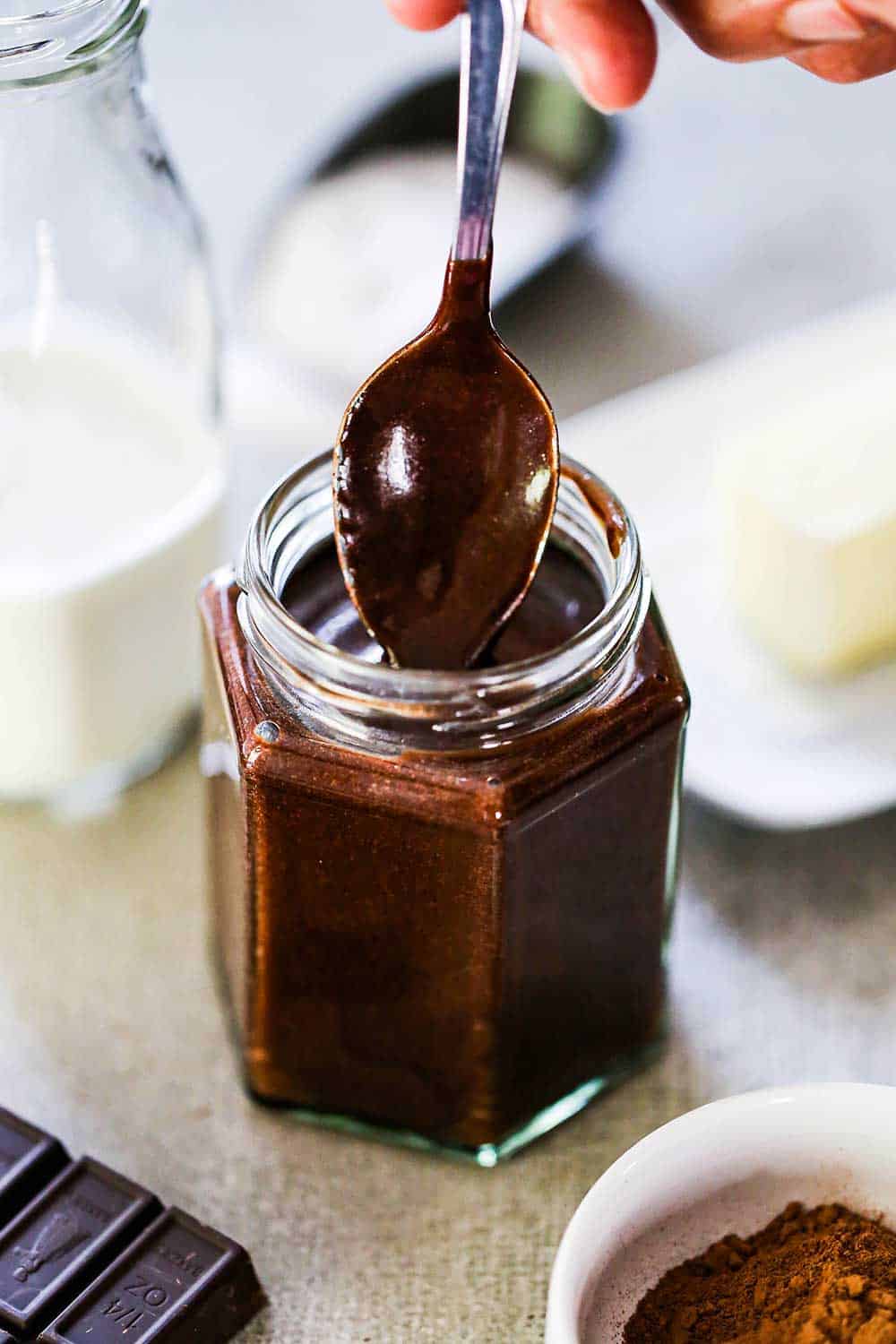 A person pulling a spoon out of a small jar filled with homemade chocolate sauce.