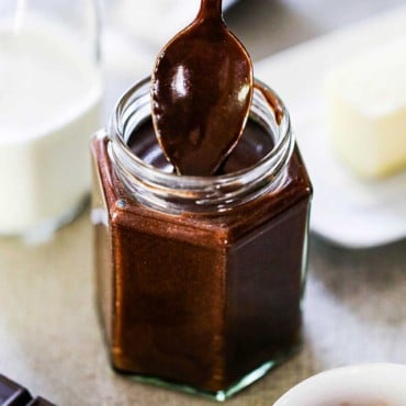 A person pulling a spoon out of a small jar filled with homemade chocolate sauce.