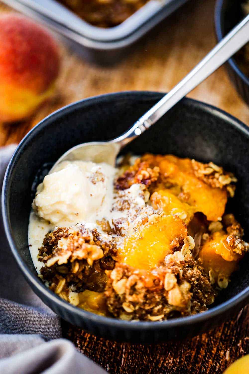 A blue dessert bowl filled with a helping of peach crisp with a scoop of melting vanilla ice cream on top.