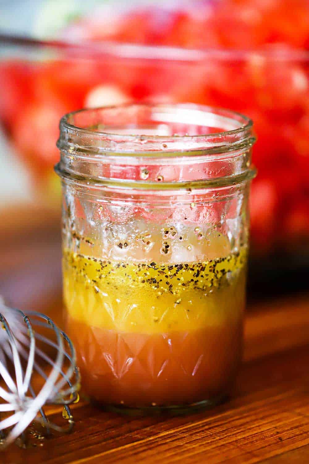 A small Mason jar filled with an apple cider vinaigrette sitting next to a bowl of chopped tomatoes. 