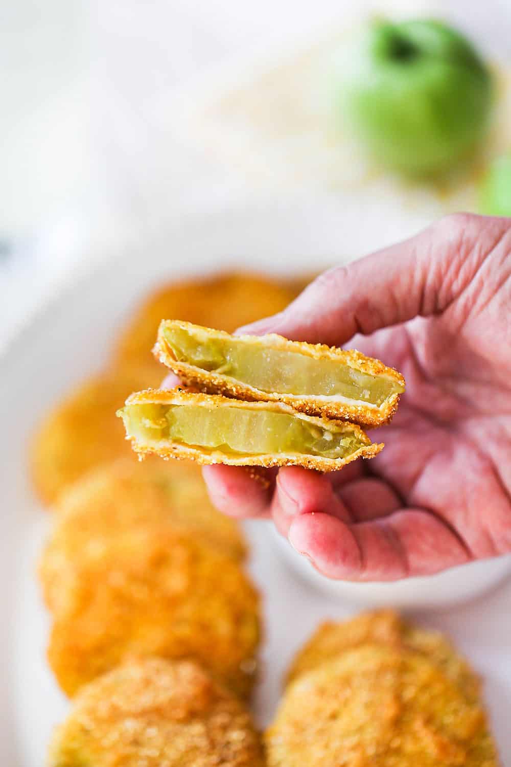 A hand holding up a fried green tomato that has been in half so the inside of the tomato is visible.