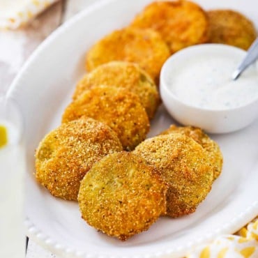 An oval white platter filled with fried green tomatoes with a small bowl of ranch dressing sitting next to them.