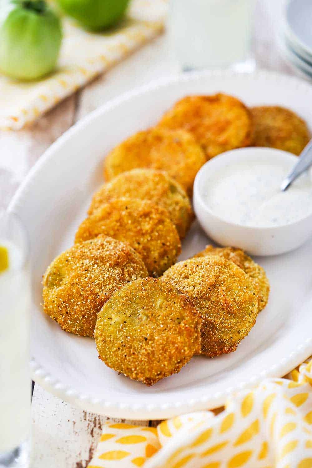 An oval white platter filled with fried green tomatoes with a small bowl of ranch dressing sitting next to them.