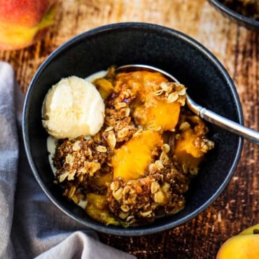 A blue dessert bowl filled with a helping of peach crisp with a scoop of melting vanilla ice cream on top.