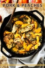 A large black cast-iron skillet filled with pan-fried pork cutlets and peaches in a savory sauce all next to several whole peaches.