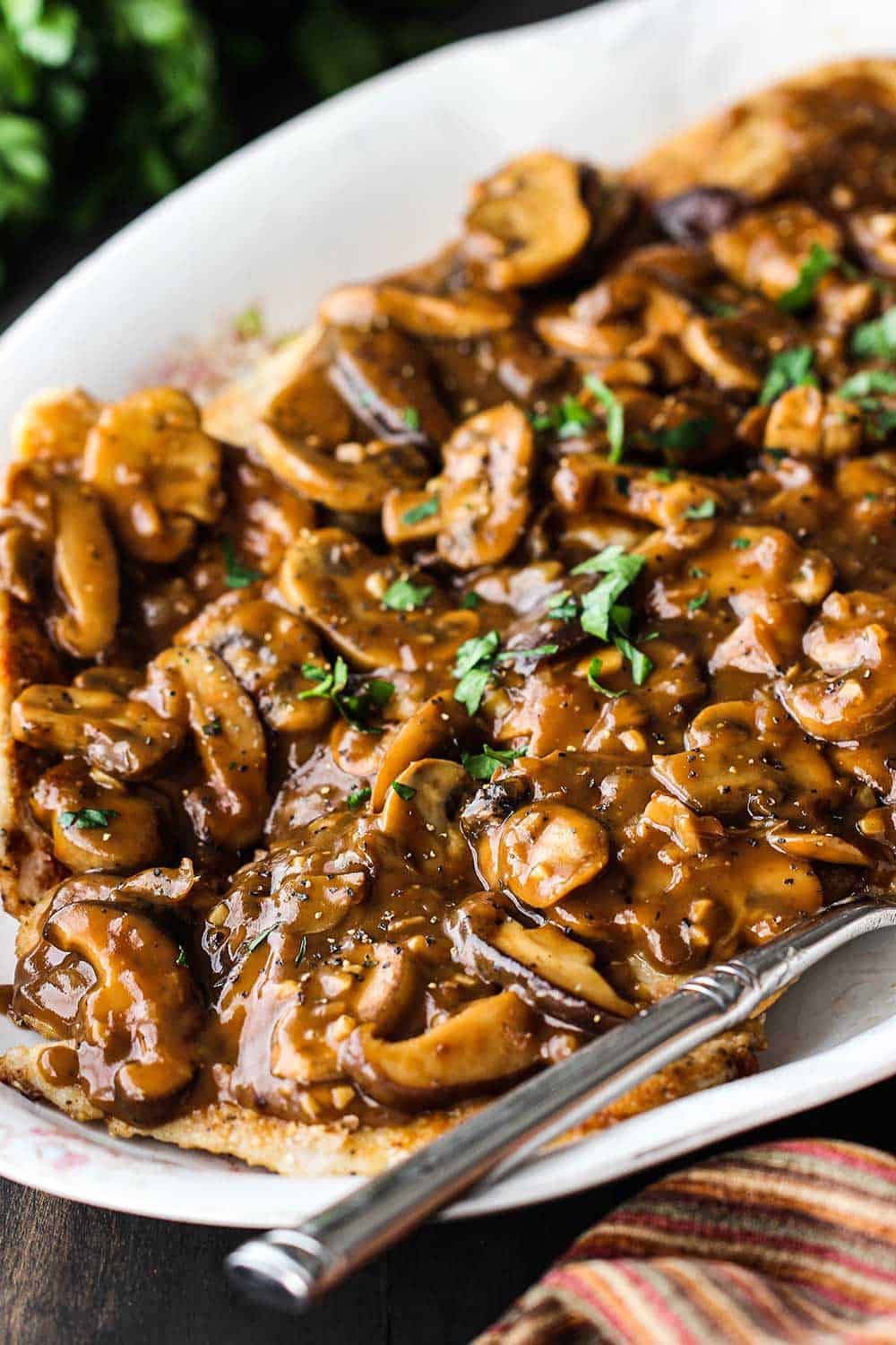 An oval white platter filled with chicken marsala with a serving spoon off to the side.