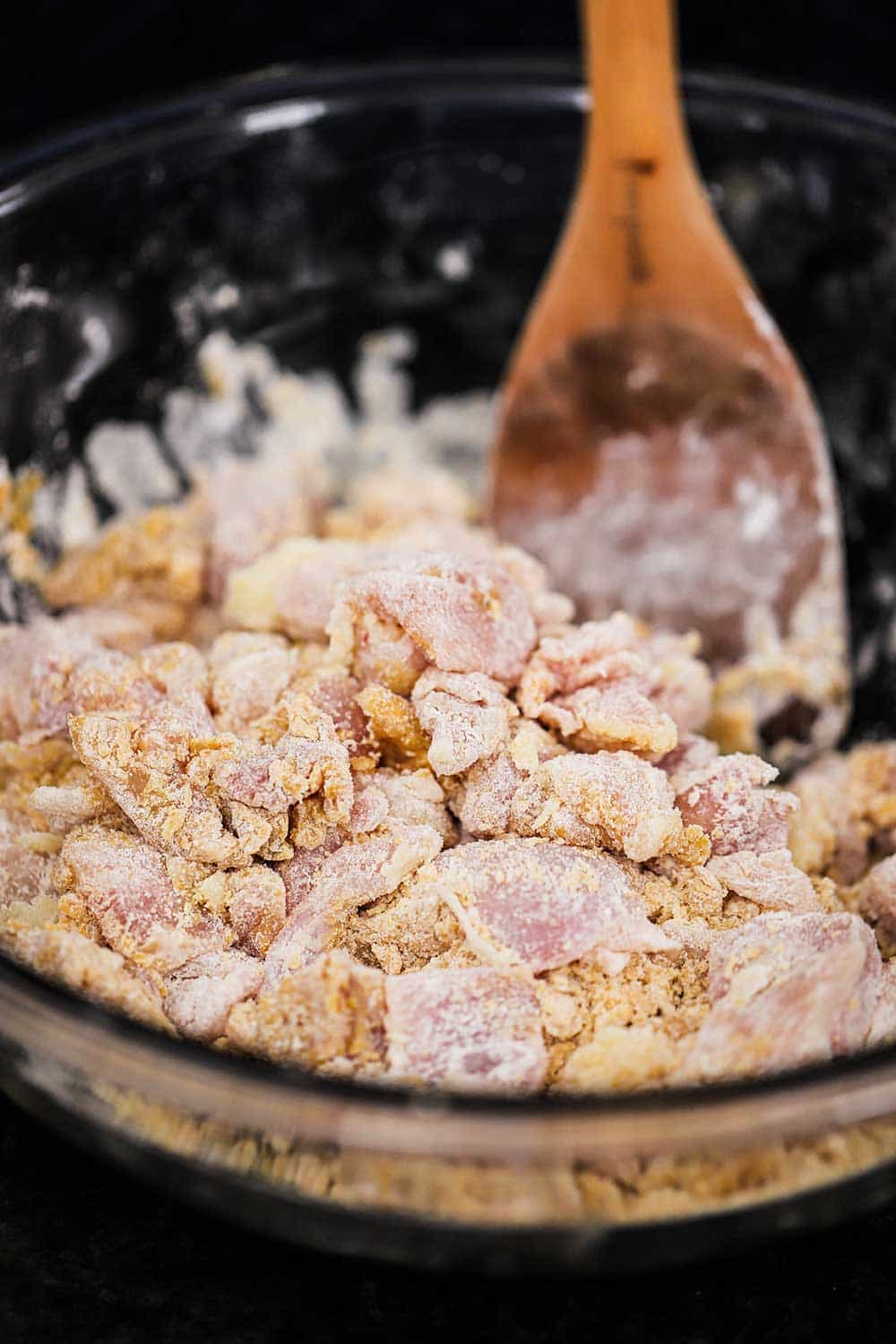 A glass bowl filled with uncooked pieces of chicken meat that has been coated with corn starch, flour, egg yolks, and seasonings. 