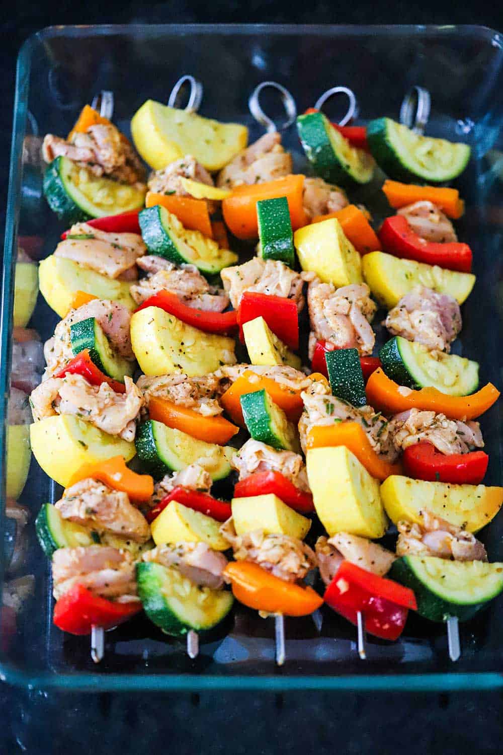 A 9x13-inch glass baking dish filled with 5 chicken and vegetable kabobs. 