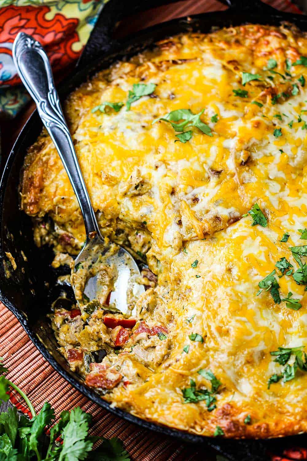 King Ranch casserole in a large cast iron skillet with a spoon in it all next to festive napkins.