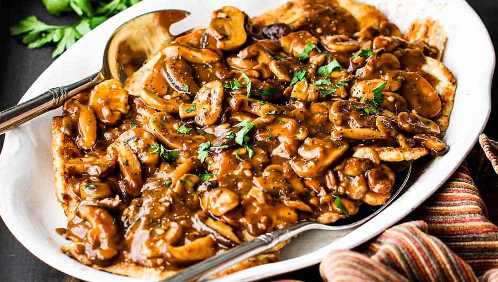 An oval white platter filled with chicken marsala with a serving spoon off to the side.