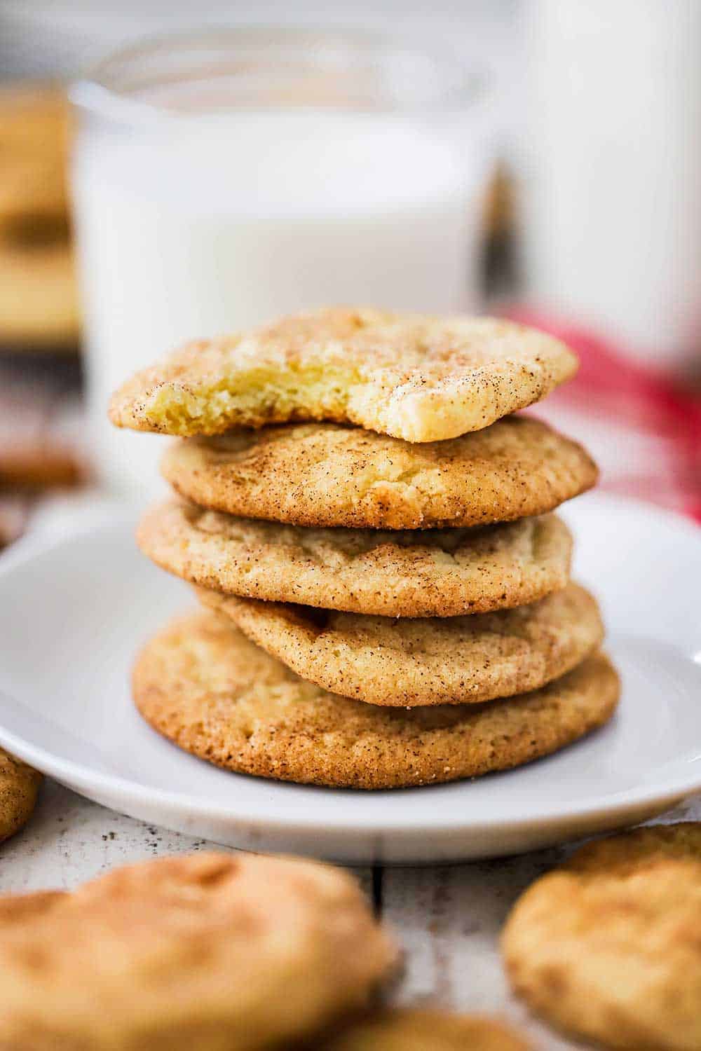 A stack of snickerdoodle cookies on a small white plate surrounded by other cookies and a glass of milk.