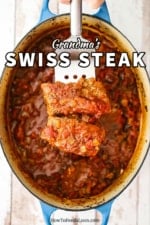 A metal spatula holding up two steak fillets covered in a red tomato sauce directly over an oval Dutch oven filled with Swiss steak.