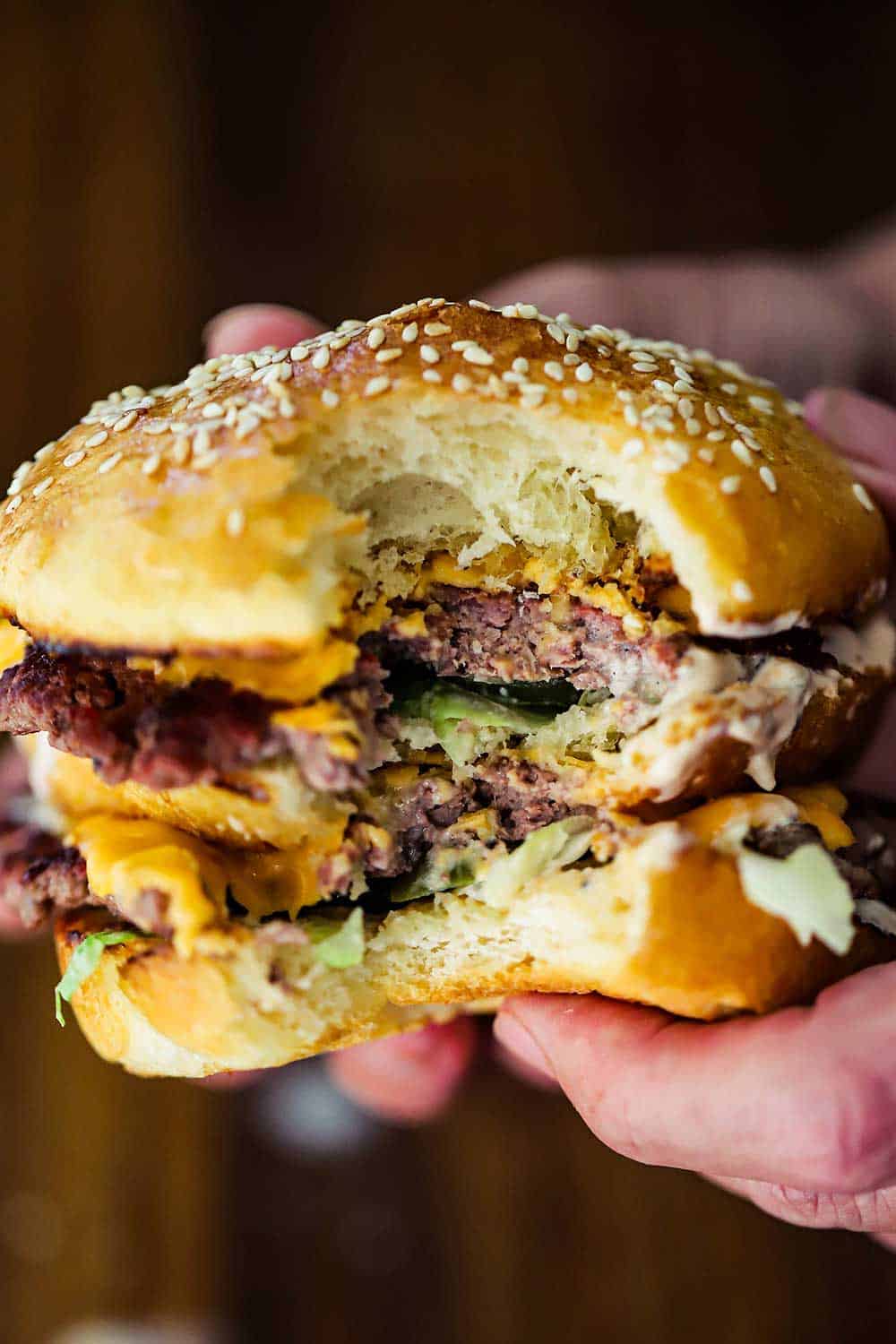 A pair of hands holding a homemade Big Mac hamburger with a bite taken out it.