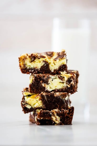 A stack of four square chocolate and cheesecake brownies on a white surface.
