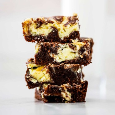 A stack of four square chocolate and cheesecake brownies on a white surface.