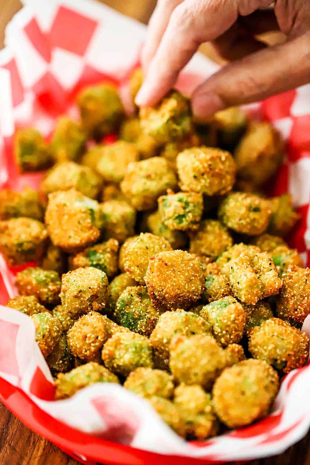 A person reaching into a basket lined with red checkered paper and filled with fried okra. 