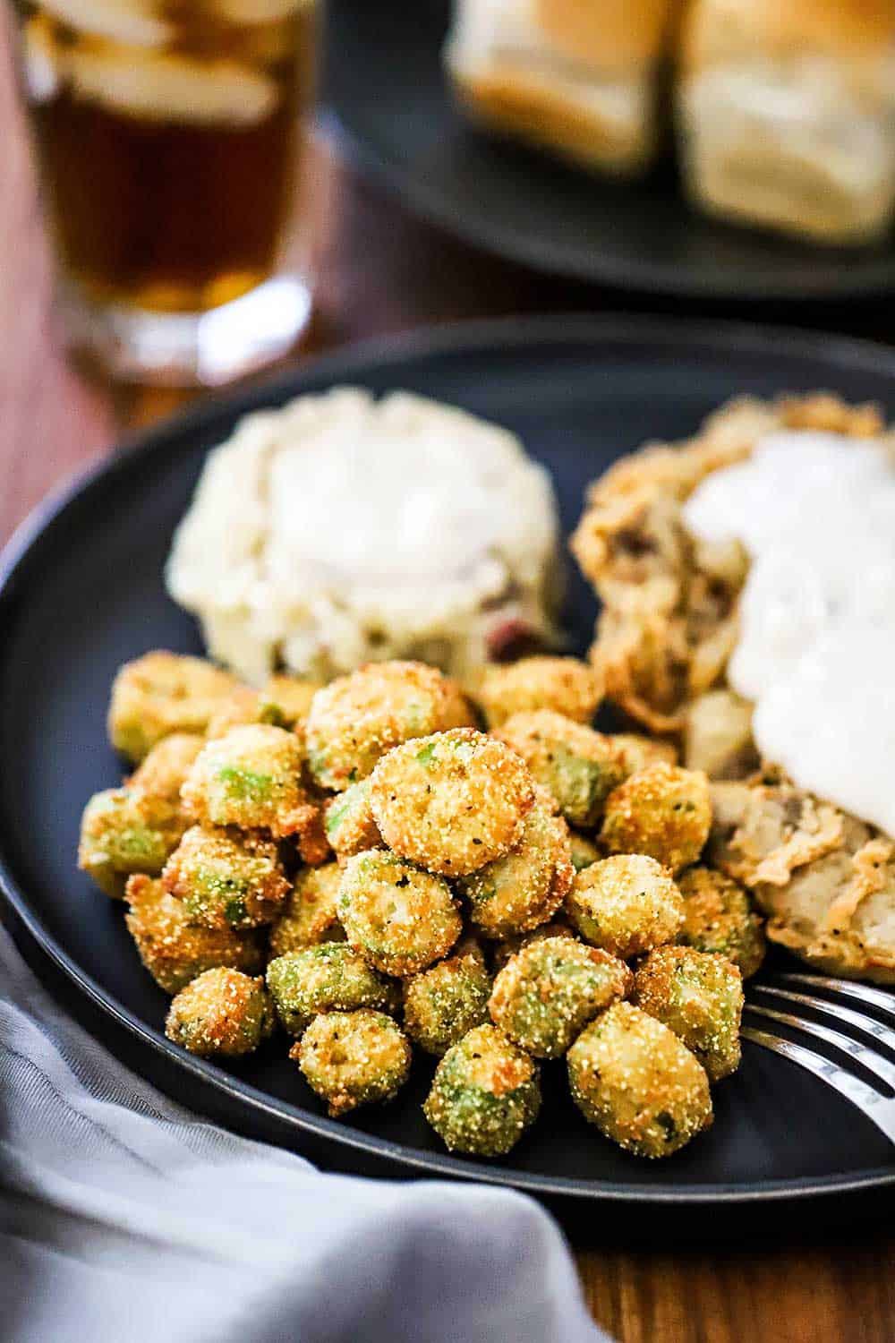 A blue dinner plate willed with chicken fried steak, mashed potatoes, both topped with gravy, all next to a pile of fried okra. 