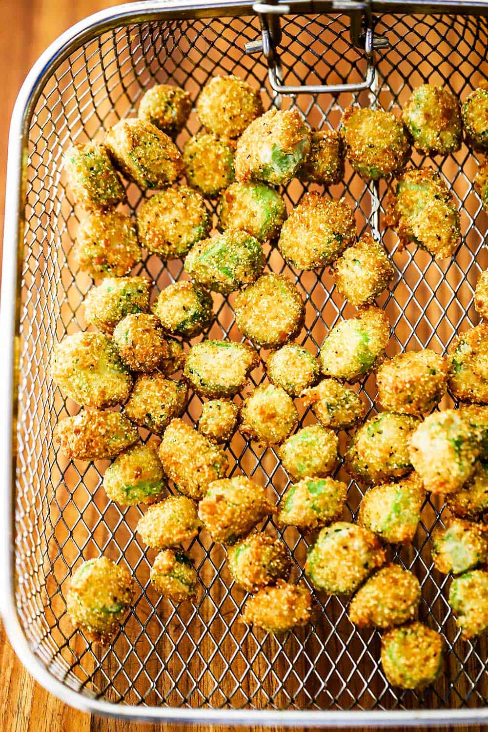 A fryer basket will with fried okra all over a wooden cutting board. 