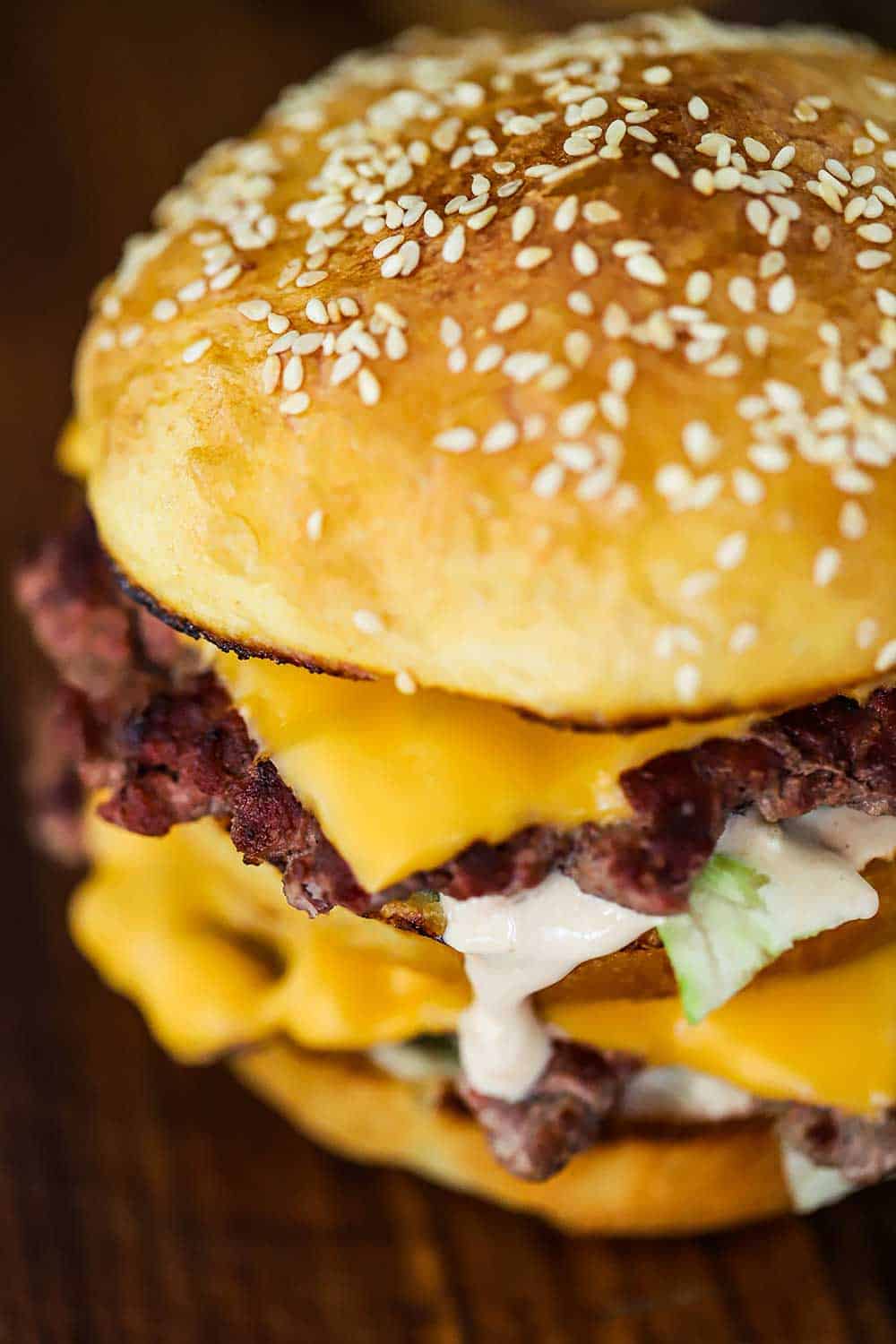 A homemade Big Mac hamburger sitting on a cutting board with Russian dressing dripping from one of the patties.