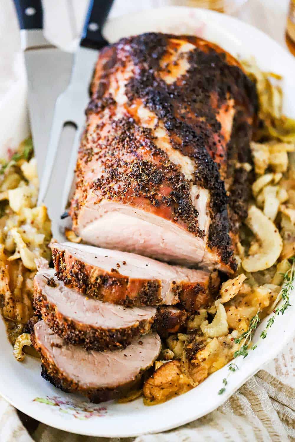 A large pork loin roast with several slices cut surrounded by roasted apples and fennel bulbs.