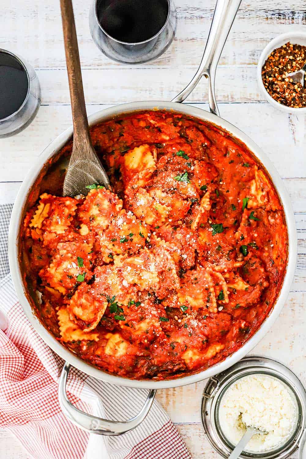 A large silver skillet filled with easy ravioli with creamy basil-tomato sauce with a wooden spoon stuck in it.