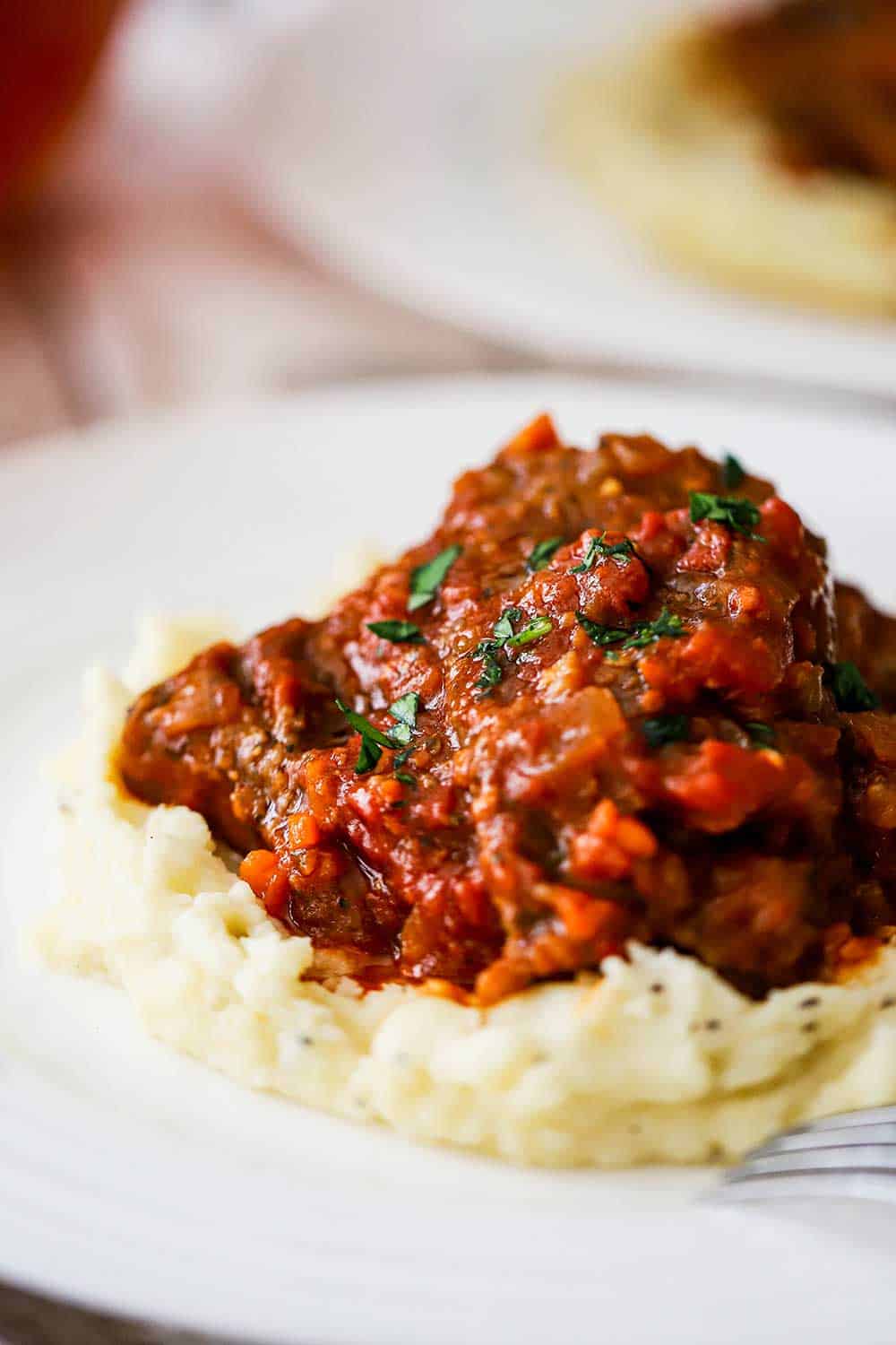 A white dinner plate filled with a bed of mashed potatoes with a helping of Swiss steak sitting on top of it.