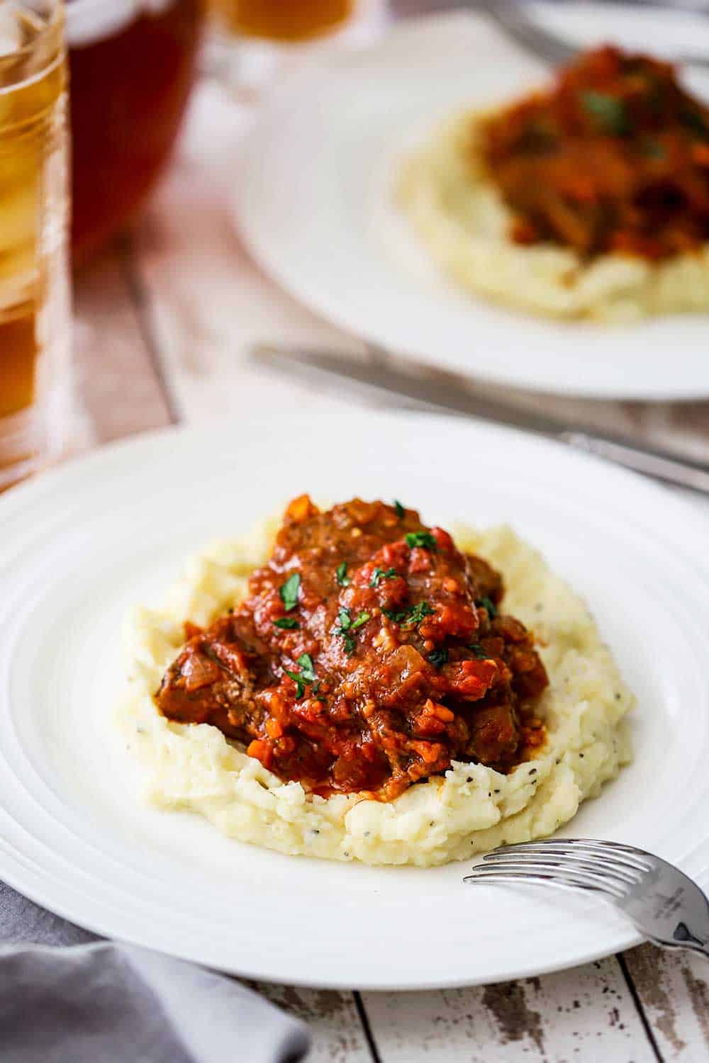 Two side by side white dinner plates filled mashed potatoes topped with a helping of Swiss steak.