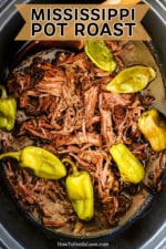 A slow-cooker filled with shredded pot roast topped with six pepperoncini peppers.