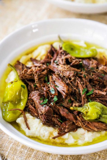 A white bowl filled with mashed potatoes topped with Mississippi pot roast.