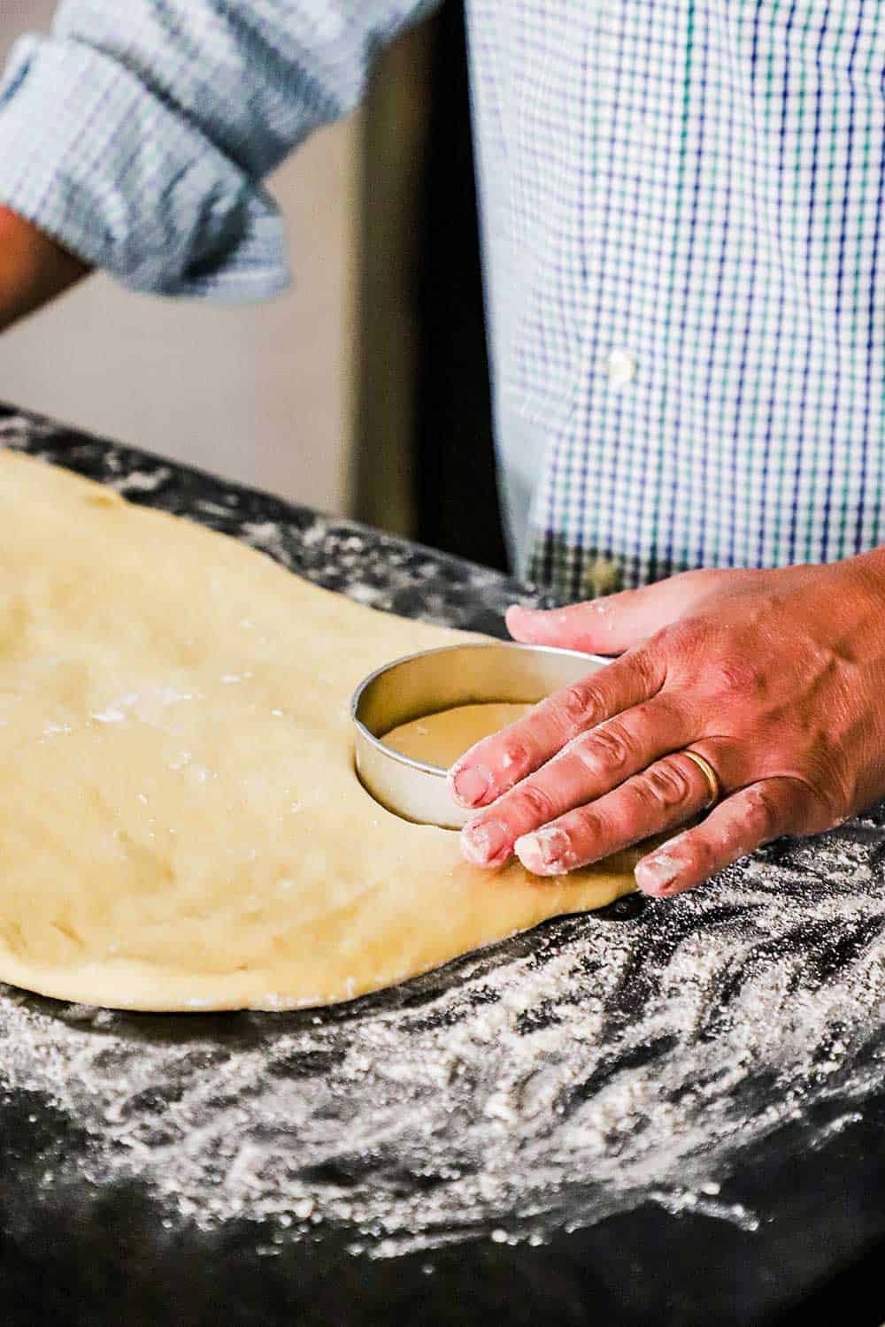 A person using a large circular cookie cutter to cut out rounds from dough that has been rolled out into a large rectangle.