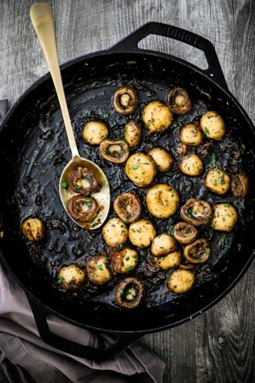 A large cast-iron skillet filled with sautéed mushrooms that have been sprinkled with fresh chopped parsley.