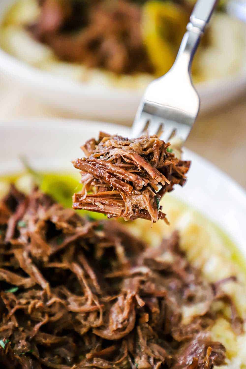 A fork holding up shredded roast beef over a bowl filled with the same.