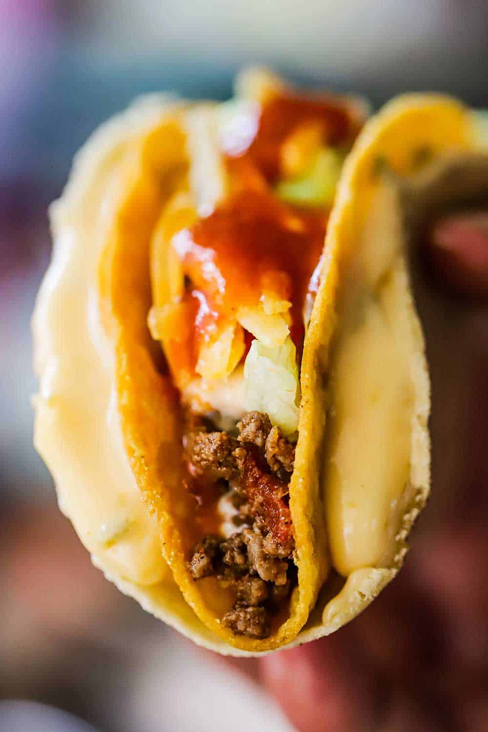 A close-up view of a crunch taco encased with a soft tortilla lined with a cheese sauce.