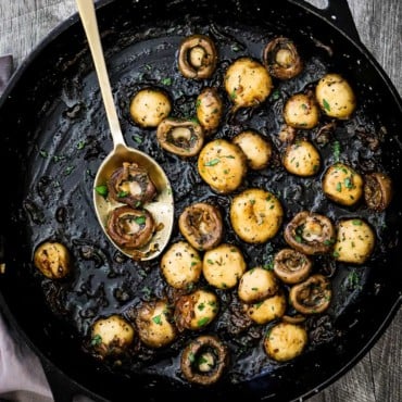 A large cast-iron skillet filled with sautéed mushrooms that have been sprinkled with fresh chopped parsley.