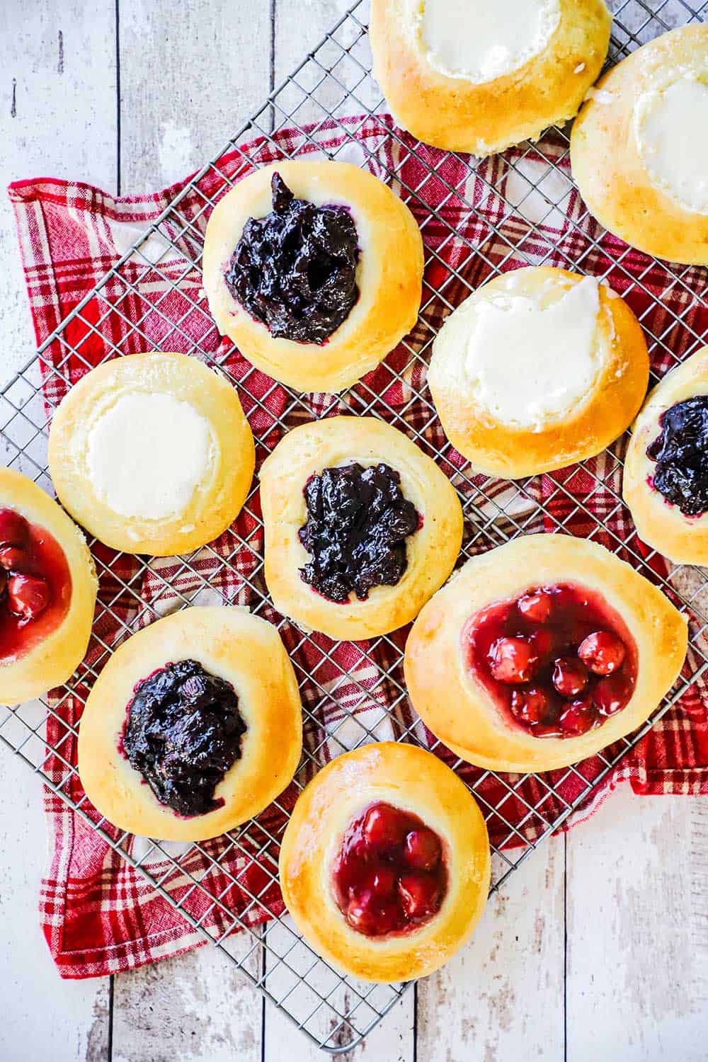 A rack that is covered with fruit-filled and cream cheese-filled Kolaches all on top of a red napkin.