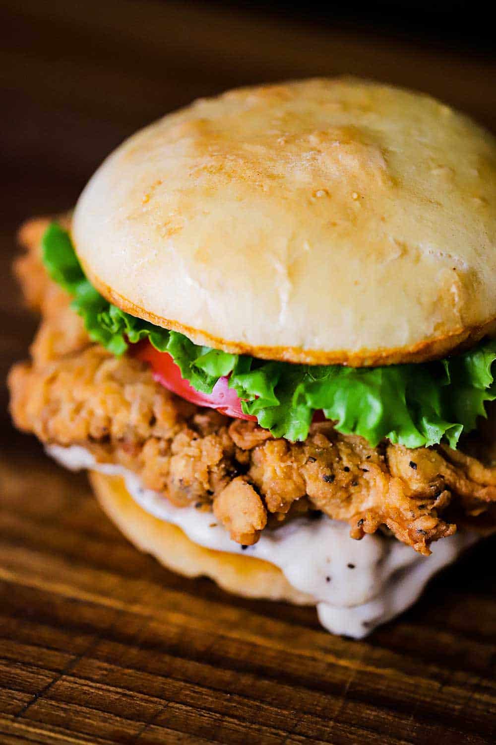 A chicken fried steak sandwich with cream gravy oozing from the bottom bun sitting on a cutting board.