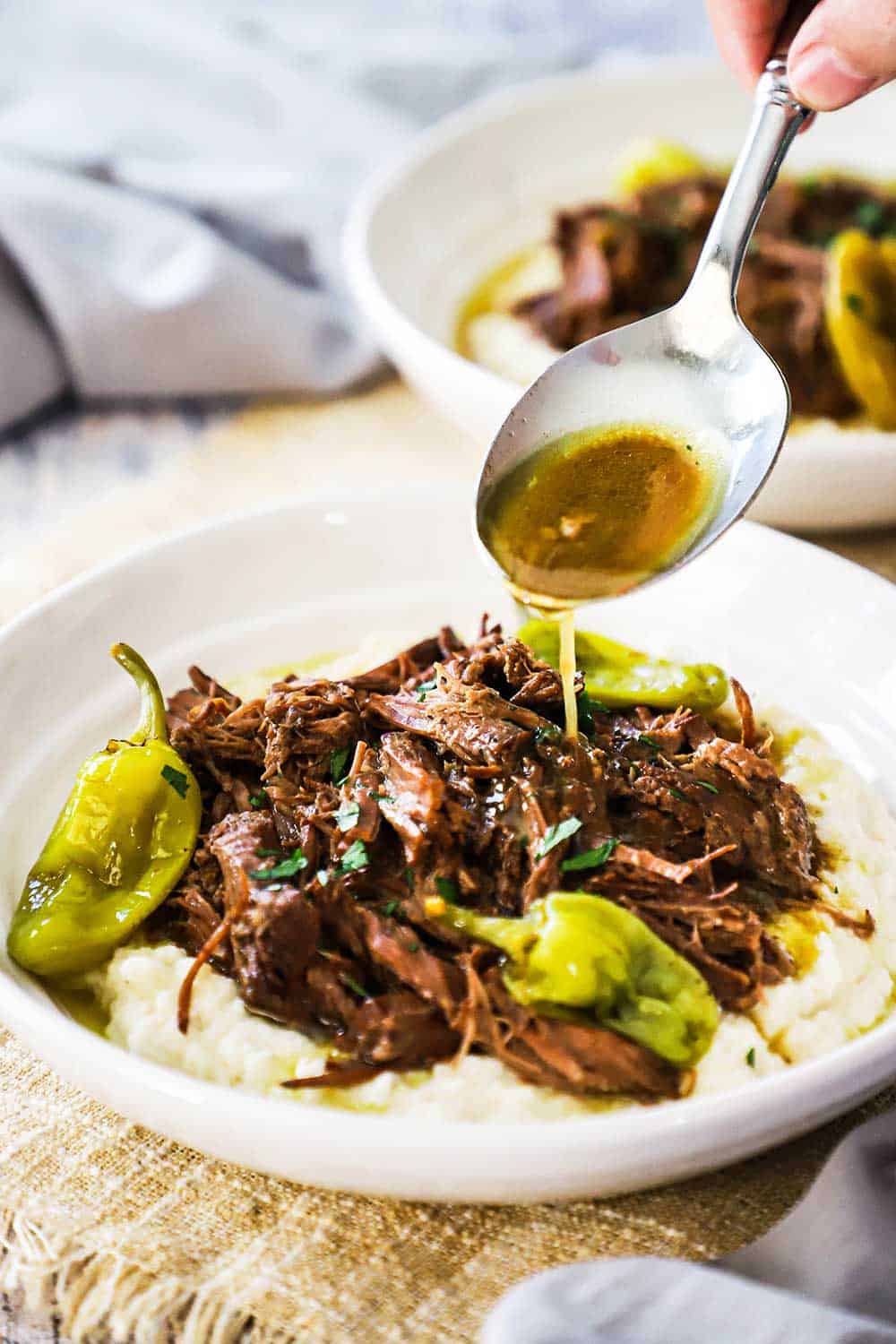 A person pouring a butter sauce over a bowl filled with Mississippi pot roast over mashed potatoes.