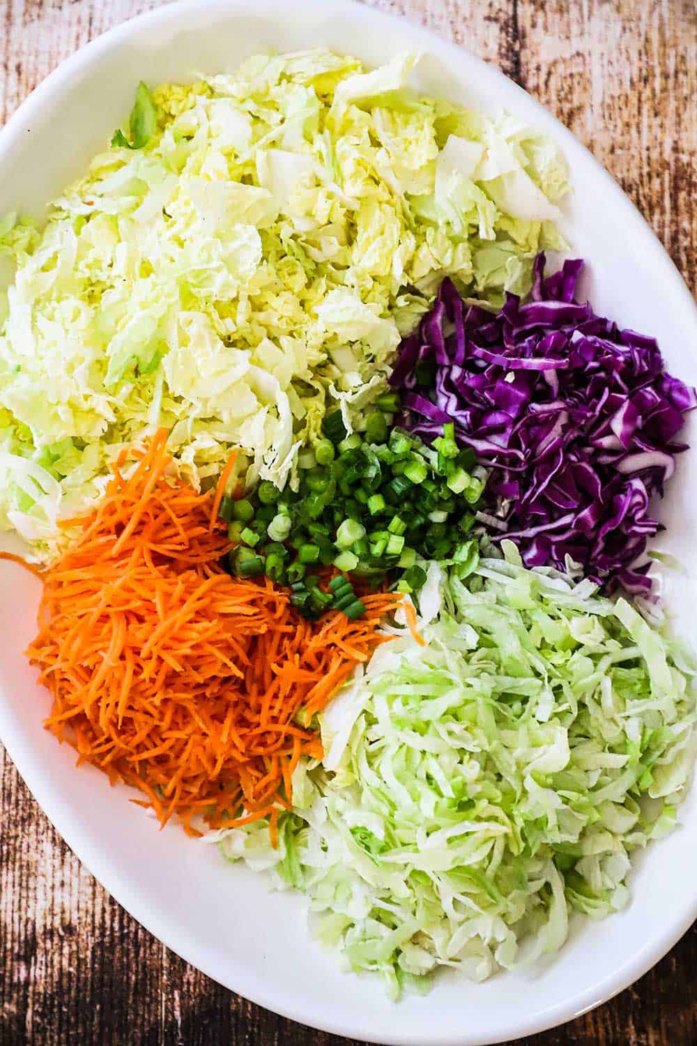 A large white oval platter filled with chopped green and red cabbage, iceberg lettuce, and shredded carrots. 