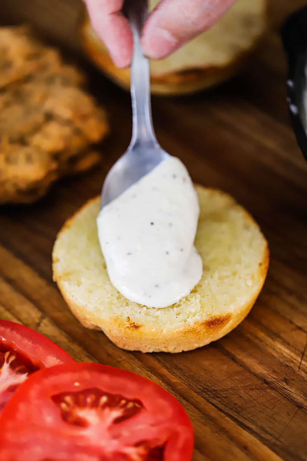 A person spooning cream gravy onto a bottom hamburger bun.