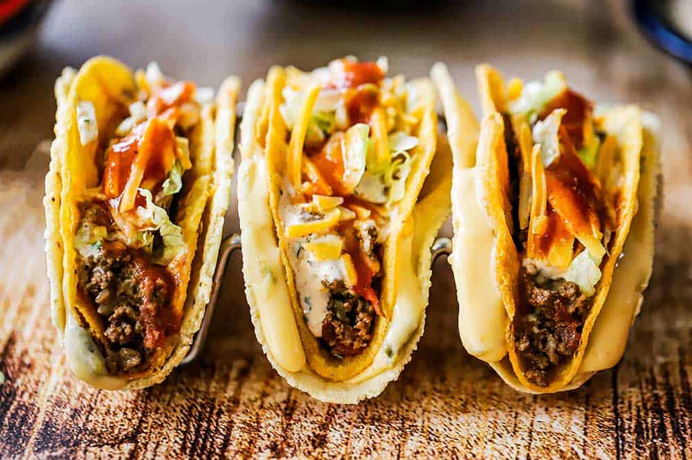 A row of three standing cheesy gordita crunch tacos on a wooden surface.