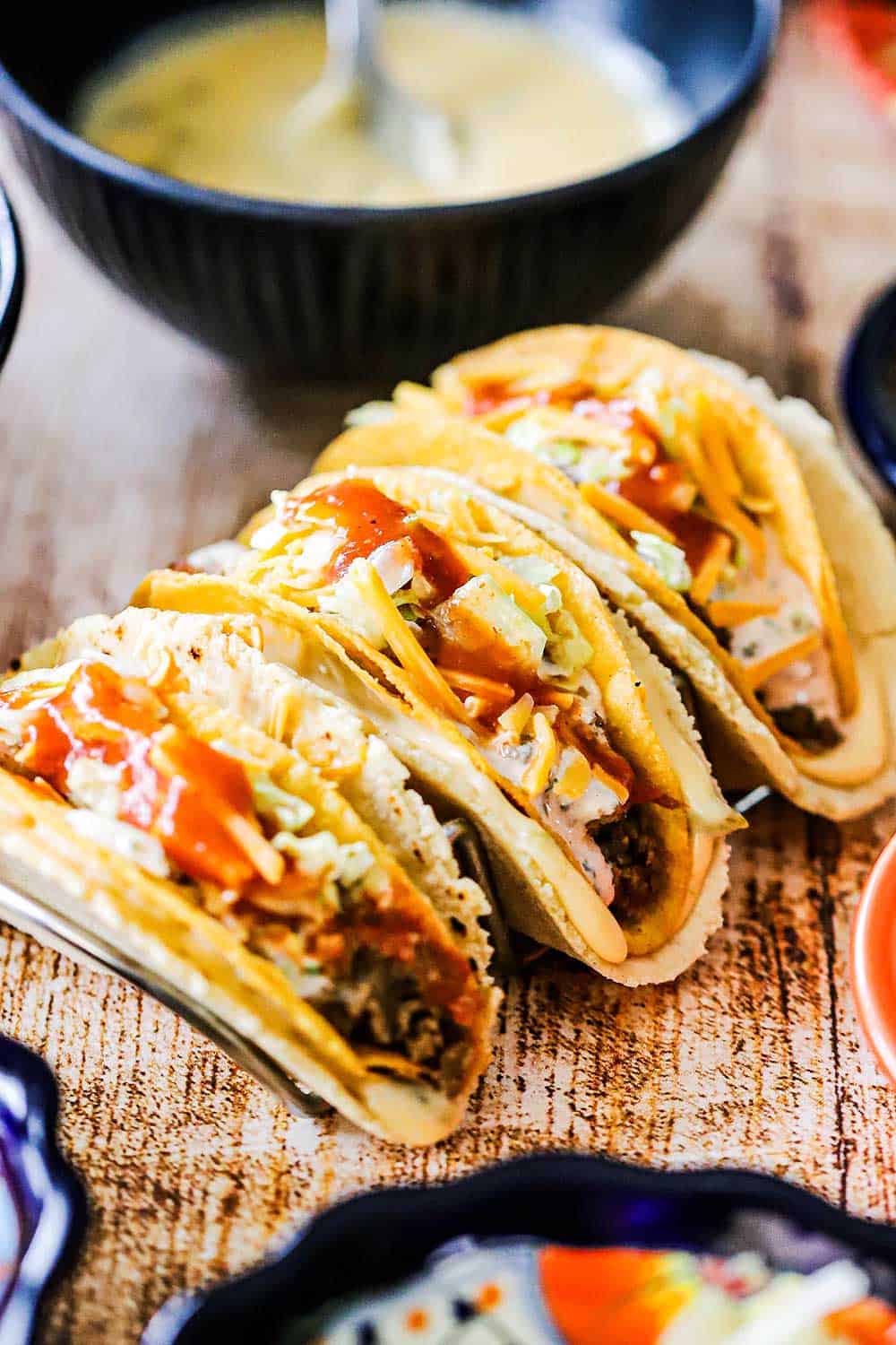 Three cheesy gordita crunch tacos sitting on a taco holder on a wooden surface.