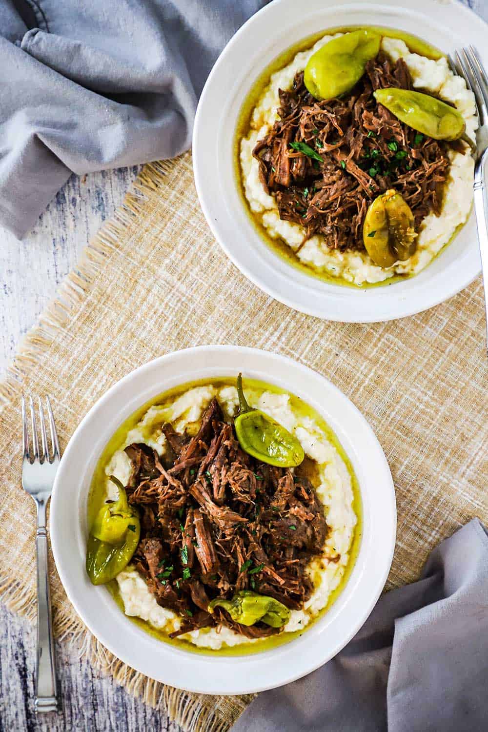 Two white bowls side by side holding mashed potatoes topped with a helping of Mississippi pot roast topped with green peppers.