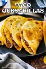 A row of taco quesadillas leaning against each other on a black serving plate.