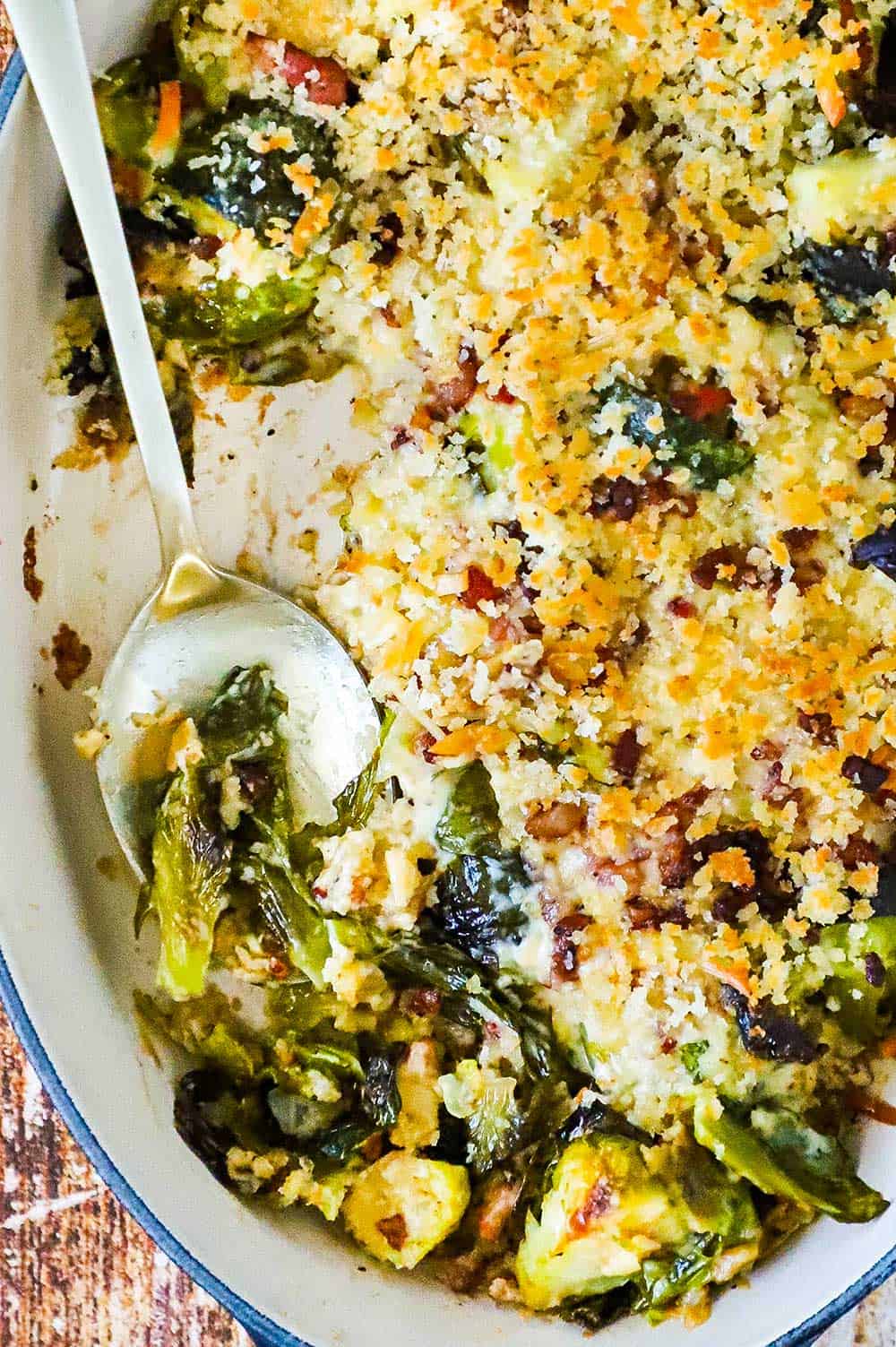 An oval baking dish filled with Brussels sprouts gratin with a spoon nestled into the dish.