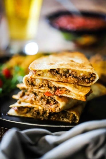 A stack of taco quesadillas that have each been cut in half all on a black dinner plate.