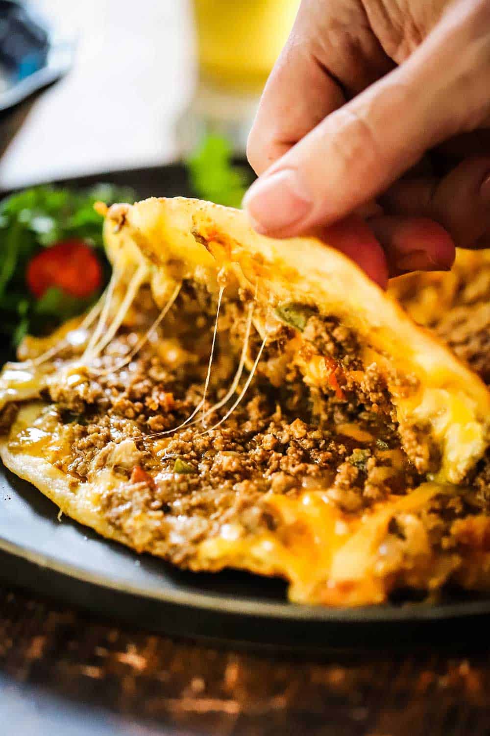 A person using his fingers to open a taco quesadilla filled with beef taco meat and melted gooey cheese. 