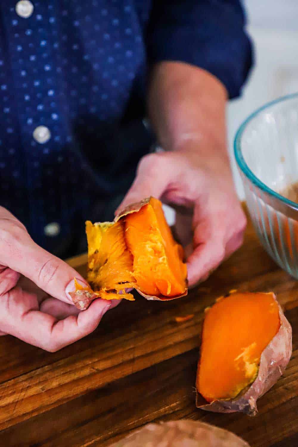 A person in a blue shirt easily pulling the skin away from a roasted sweet potato. 