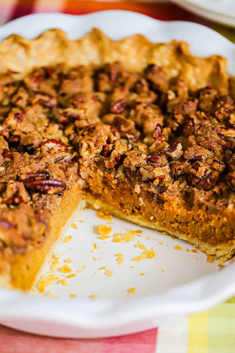A sweet potato pie with pecan topping in a white pie dish with a large slice missing on one side of the dish. 